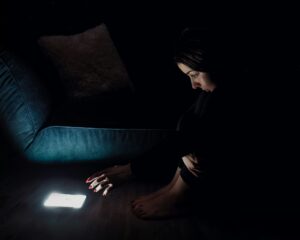 Image of a person in a dark room reaching for an illuminated phone.