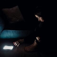 Image of a person in a dark room reaching for an illuminated phone.